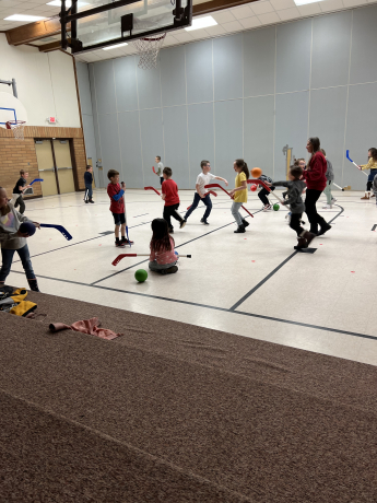 Students run in the gym while playing hockey horse tag