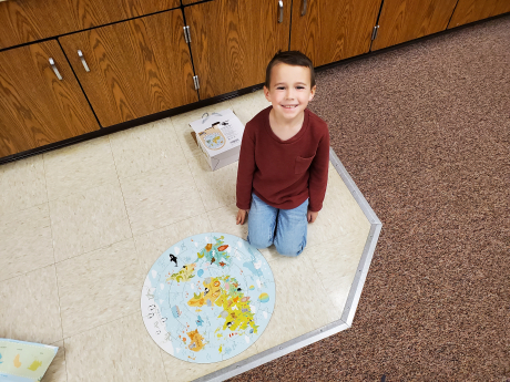 A students smiles with his completed puzzle of the world