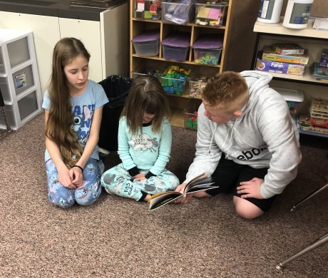 A fifth grade boy reads to two girls