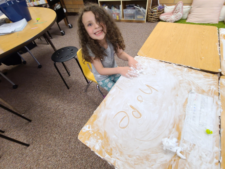 A student smiles with shaving cream on her desk