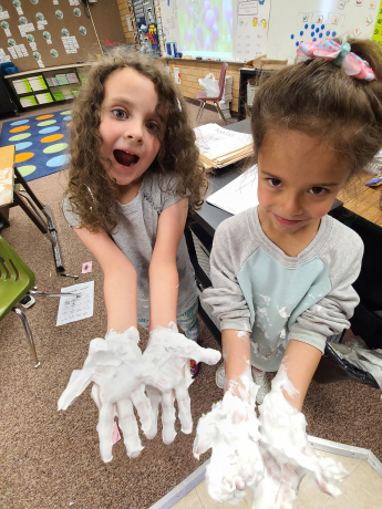 2 girls show off their hands covered in shaving cream