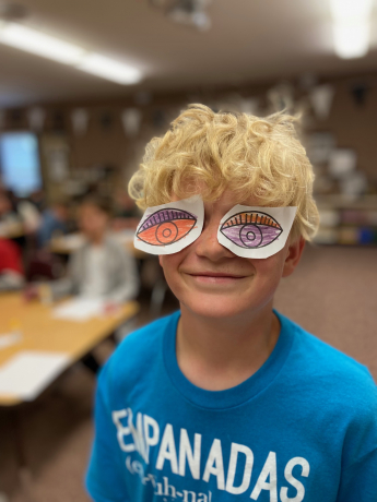 A boy poses with large paper eyes, looking like a picasso painting himself