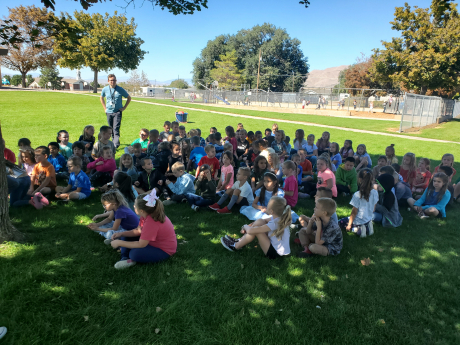 Students sitting on the grass listening to Mr. Richins read