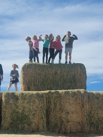 Students flex their muscles on the top of a large haystack